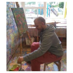 Ein man sitzt vor einer Leinwand und malt ein Bild.