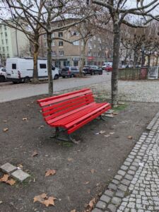 Eine rote Parkbank auf einem Platz.